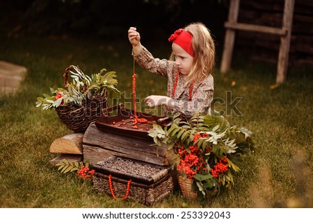 child girl making rowan berry beads in autumn garden