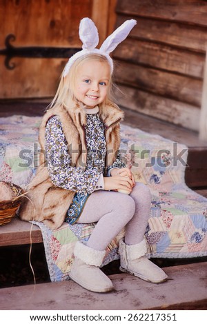 cute happy child girl wearing bunny ears for easter sitting at country house