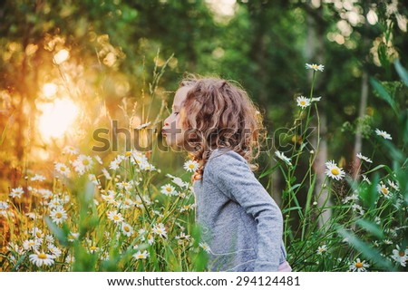 cute curly child girl smells flowers on the walk in summer sunny day