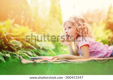 cute child girl reading book and dreaming in summer garden