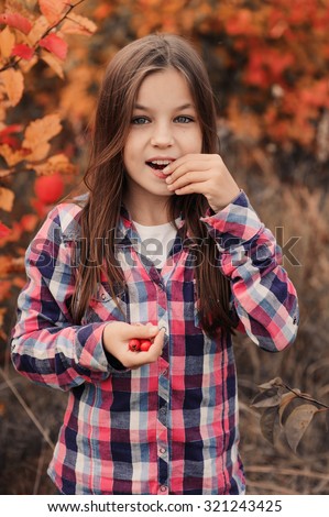 adorable happy kid girl in plaid shirt eating red wild berries on the autumn walk in warm day