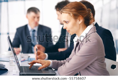 Young business woman working on her laptop with her colleagues at the background.