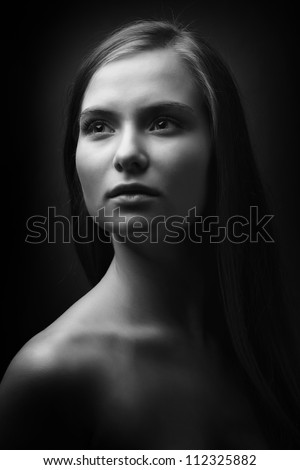 Classical portrait of young woman with long hair and bare shoulders looking left. Black and white photo