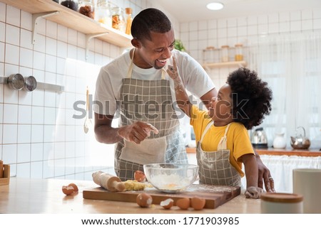 African family have fun cooking baking cake or cookie in the kitchen together, Happy smiling Black son enjoy playing and touching his father nose with finger and flour while doing bakery at home.