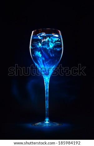 Amazing blue cocktail with ice cubes in high glass. Blue curacao liquor. Magic lights and shadows.