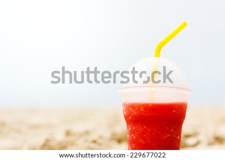 Red fruit icy cocktail in beach sand. Traveling and relaxing concept. Space for your text.