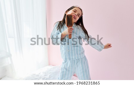 Similar – Image, Stock Photo Little girl singing holding headphones cord imitating herself a real singer. Child having fun jumping dancing listening to music on bed in bedroom at home