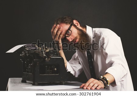 Handsome young hipster businessman thinking and writing with vintage typewriter. Old fashion style.