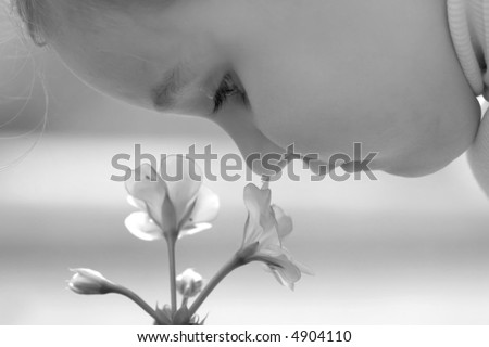 Little girl smell flower over defocused background. Black-and-white variant