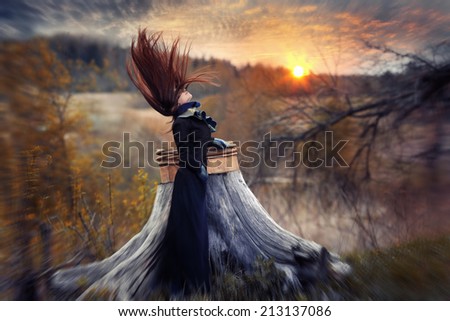 silhouette of a girl in black with hair developing on a background of autumn landscape and sunset