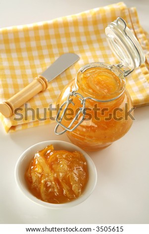 bottle with orange jam, plate, knife and fresh oranges on back, soft focus