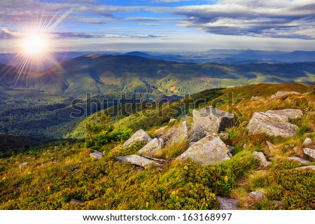 autumn landscape. valley with stones on the hillside. forest on the mountain covered with red and yellow leaves. over the mountains the beam of light falls on a clearing at the top of the hill.