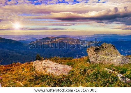 autumn landscape. valley with stones on the hillside. forest on the mountain covered with red and yellow leaves. over the mountains the beam of light falls on a clearing at the top of the hill.