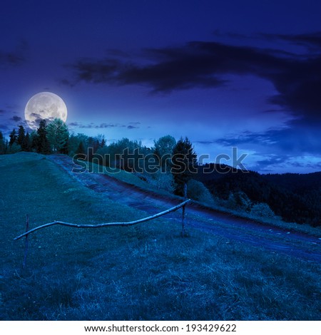 summer landscape. fence near the meadow path going up on the hillside. forest in fog on the mountain at night in moon light