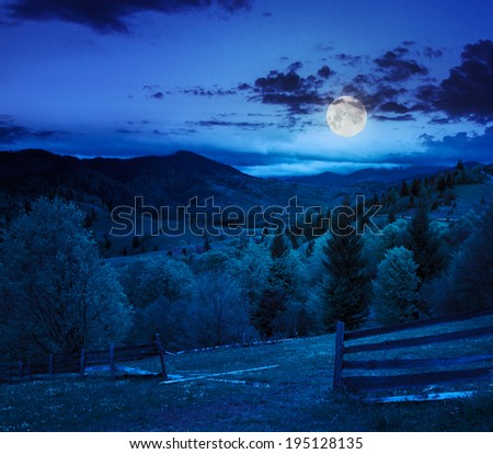 summer landscape. fence near the meadow path on the hillside. forest in fog on the mountain at night