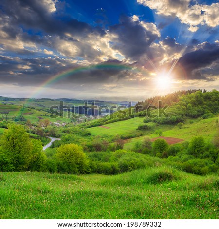 summer landscape. village on the hillside. forest on the mountain light fall on clearing on mountains at sunset with rainbow