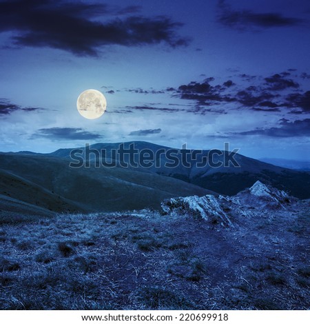 mountain landscape. valley with stones on the hillside. forest on the mountain under the beam of light falls on a clearing at the top of the hill. at night in full moon light