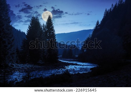mountain river with stones and moss in the forest near the mountain slope at night in full moon light