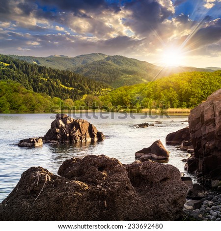view on lake with rocky shore and some boulders near forest on mountain  with high vista far away in sunset light