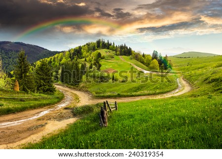 composite autumn landscape. fence near the cross road on hillside meadow in mountains. few fir trees of forest  on both sides of the road in morning light with rainbow