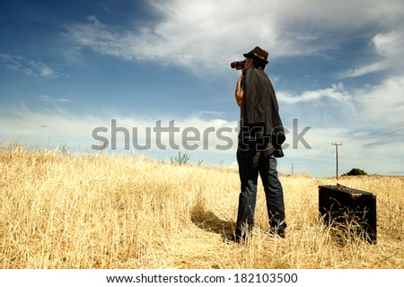 Man standing in a field watching with binoculars