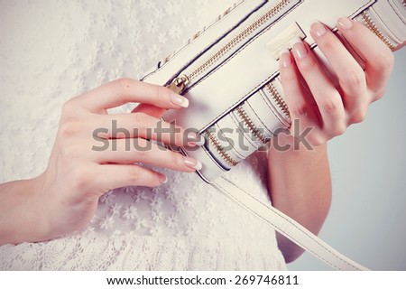 Female hands with manicure hold an open small white handbag