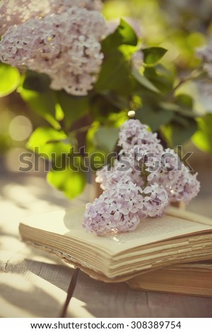 Branches of a lilac and old books on a wooden table.