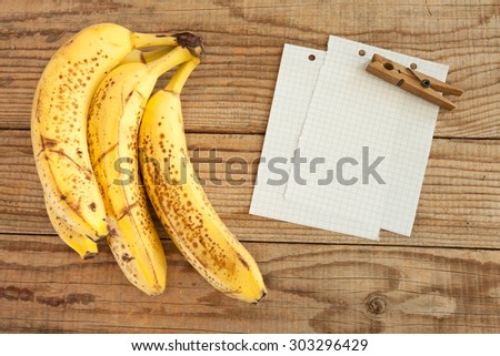 block note on wooden table next to four bananas