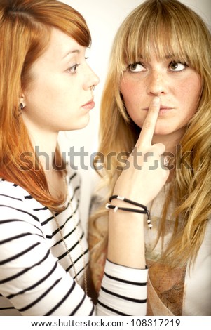 red haired and blond girl sign to shut up with finger