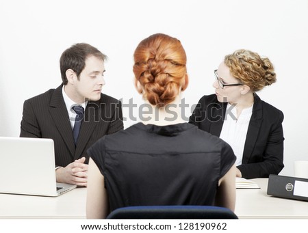 A male and female business executive conducting a job interview with a redhead woman applicant who is sitting in the foreground with her back to the camera