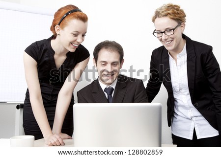 Three happy business colleagues, a business man and two women, looking at the screen of a laptop together and smiling in amusement