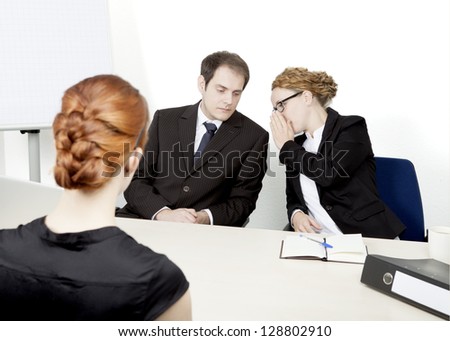 View over the shoulder of a redhead female applicant of two personnel managers conducting a job interview whispering amongst themselves about their impression and decision