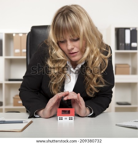 Curly Haired Corporate Woman Covering House Miniature Top on Table.