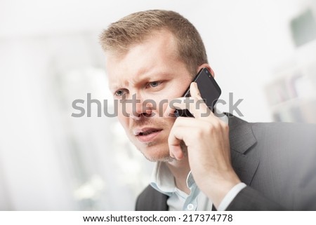 Anxious businessman taking a mobile phone call frowning with a worried expression as he listens to the conversation