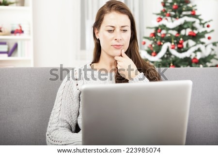 young girl is surfing with laptop at christmas on sofa with christmas tree in background