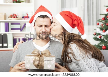boyfriend looks skeptical to his christmas gift while his girlfriend give him a kiss