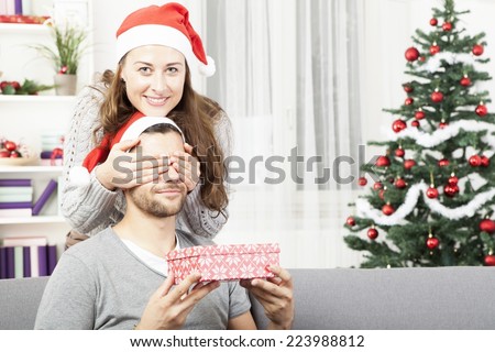 young girl is giving her boyfriend a christmas gift in front of christmas tree