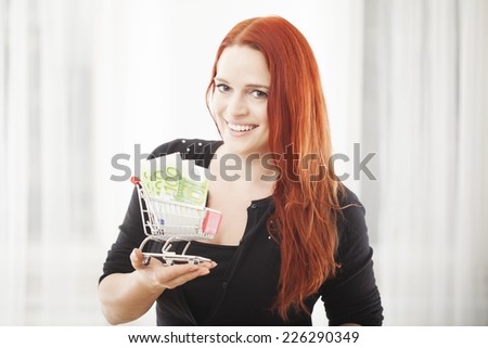 young happy girl with mini shopping cart trolley with euro bank note smiling