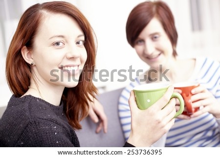 Two happy young female friends with coffee cups enjoying a conversation in the living room at home