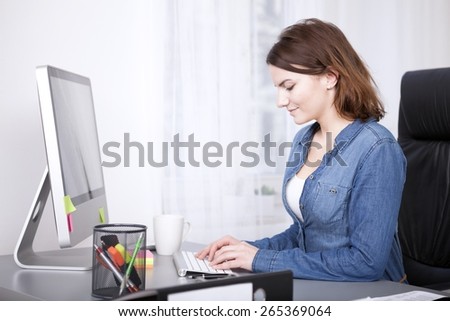 Smiling businesswoman inputting data to her desktop computer sitting typing on the keyboard, side view