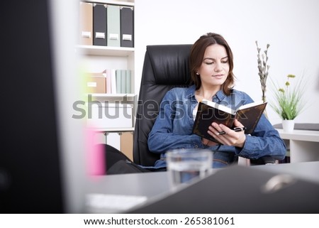 Young Office Woman in Denim Fashion Reading a Book Seriously While Sitting on her Chair at her Office.