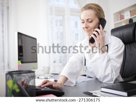 Adult Female Doctor Sitting at her Office While Dialing a Telephone Number of her Patient.