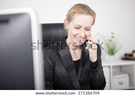 Close up Happy Blond Businesswoman in Black Suit Talking to Someone Through Mobile Phone While Sitting at her Office.