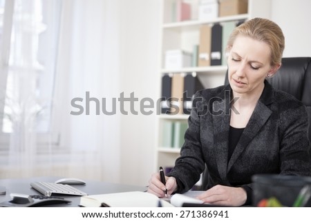 Close up Adult Businesswoman in Black Suit, Sitting at her Desk, Writing on Paper Seriously.