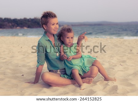 Special toned photo of young mother and daughter together on the beach dressed in similar clothes view 2