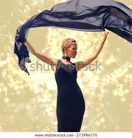 Beautiful young woman in black evening dress holding black fabric at wind with glitter and flare special effect view 3