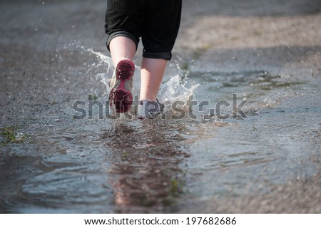 Closeup of water splashing up from a little girl\'s shoes as she runs through a puddle in the street, selective focus on the stream of water behind her shoe.
