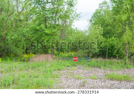 A metal gate with a stop sign blocks the way into a beautiful wooded land with green trees and wild yellow flowers
