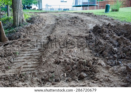 A backyard is scarred by dirt tracks from a front-loader or bulldozer