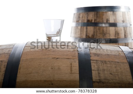 Whiskey glass on a whiskey barrel with a second barrel in the distance, isolated on white, selective focus on glass